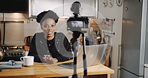 Happy smiling young beautiful black vlogger woman filming new video using professional camera at home table slow motion. photo