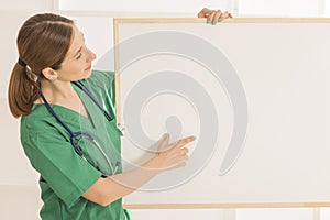 Happy smiling young beautiful female doctor showing blank area for sign or copyspace