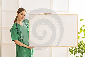 Happy smiling young beautiful female doctor showing blank area for sign or copyspace