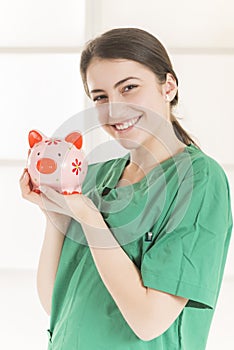 Happy smiling young beautiful female doctor with stethoscope holding pink piggy bank