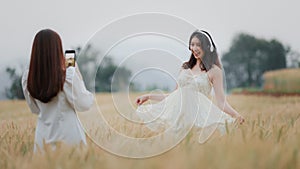 Happy smiling young beautiful woman wearing white dress taking selfie and headphone wireless while walking in the golden barley