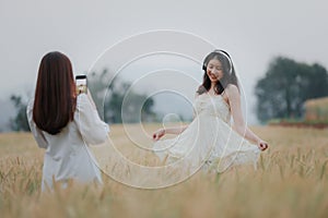 Happy smiling young beautiful woman wearing white dress taking selfie and headphone wireless while walking in the golden barley