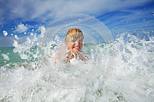 Boy play in ocean wave with water splashes during vacations