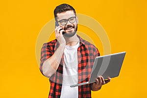 Happy smiling young business man in casual with a laptop sitting at floor calling with smart phone