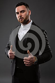 Happy smiling young businessman with raised thumb gesture, photo on dark background