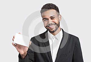 Happy smiling young businessman showing blank card, isolated over gray background. Handsome man with white card