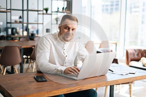 Happy smiling young businessman is typing on laptop computer at the desk in home office