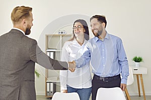 Happy, smiling young couple exchanging handshakes with professional real estate agent