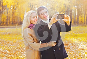Happy smiling young couple together taking picture self portrait on smarphone in sunny autumn