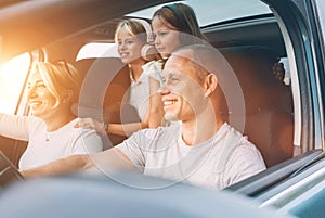 Happy smiling young couple with two daughters inside car during auto trop. They are smiling, and laughing during a road trip.