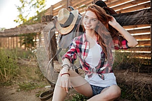 Happy smiling young cowgirl resting at the ranch fence