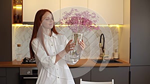 Happy smiling young creative woman decorating kitchen with dried flowers standing at table.