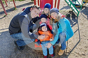 Happy smiling young family of five at children`s playground in park