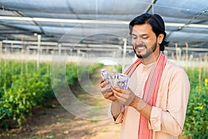 Happy smiling young farmer at greenhouse couting money or currency notes - concept of successful business, agronomy and