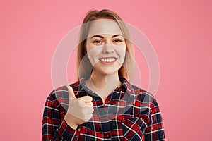 Happy smiling young female raises thumb up, demonstrates like sign, approves something, shows that she is satisfied with it, being