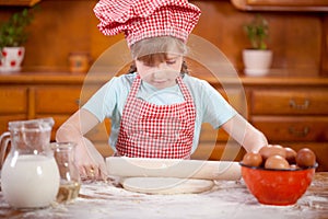 Happy smiling young girl chef in kitchen making dough