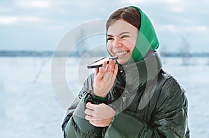 A happy smiling young girl talking on a mobile phone in a snowy winter park. A beautiful laughing girl with a mobile phone in a wi