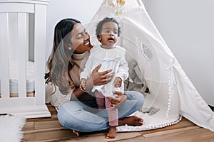 Happy smiling young Indian mother playing with black baby girl daughter. Family mixed race people mom and a kid together hugging