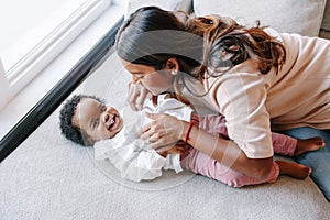 Happy smiling young Indian mother playing with black baby girl daughter. Family mixed race people mom and a kid together hugging