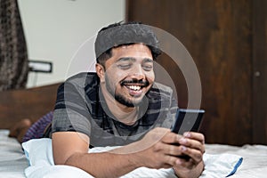 happy smiling young man busy using mobie phone at night on bed - concept of using dating application, social media and