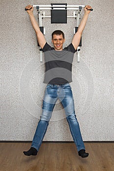Happy smiling young man doing pull-up exercises on horizontal bar at his home