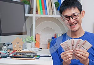 Happy smiling a young man holding money fans in hands. Cheerful gambler getting big cash prize at online working