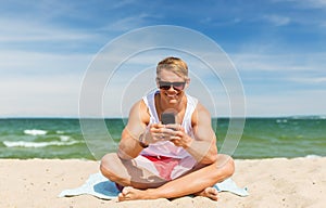 Happy smiling young man with smartphone on beach