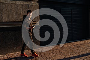 Happy smiling young man using modern smart phone while standing at crosswalk at the sunset in city center