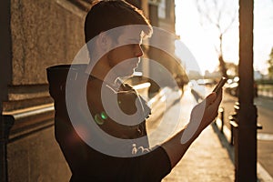 Happy smiling young man using modern smart phone while standing at crosswalk at the sunset in city center