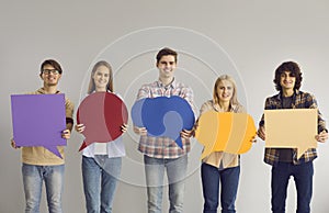 Happy smiling young men and women holding multicolored empty mockup speech bubbles