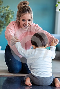 Happy smiling young mother playing with little baby on the floor at home