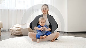 Happy smiling young mother teaching her little baby son doing yoga asana while practising yoga. Family healthcare, active