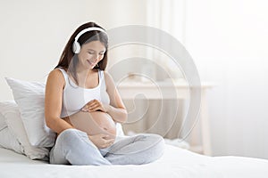 Happy smiling young pregnant woman listening to music in headphones