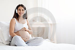 Happy smiling young pregnant woman listening to music, using headphones