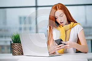 Happy redhead girl send an sms message to friend while working at modern office