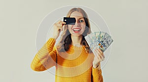 Happy smiling young 20s caucasian woman holding plastic credit bank card and cash money in dollar bills