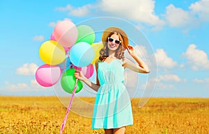 Happy smiling young woman with an air colorful balloons enjoying a summer day on field blue sky background