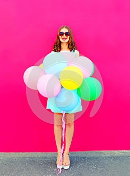 Happy smiling young woman with an air colorful balloons having fun in summer over a pink background