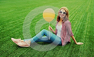 Happy smiling young woman with balloon sitting on the grass in summer park