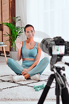 Happy smiling young woman blogger with camera on tripod recording online yoga class at home