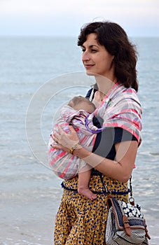 A happy smiling young woman carrying her newborn baby in a sling.