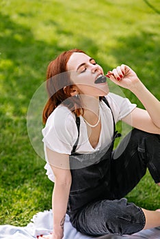 Happy smiling young woman eating cherry of the park lawn