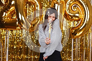 Happy smiling young woman in gray vintage knitted sweater celebrates New Year with fireworks against the background of golden