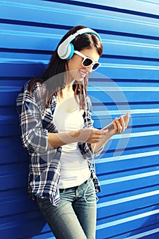 Happy smiling young woman listens to music in headphones and using smartphone