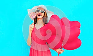 Happy smiling young woman with lollipop, pink heart shaped air balloons on colorful blue background