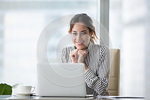 Happy smiling young woman looking at laptop screen.