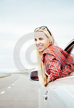 Happy smiling young woman looks out from car window