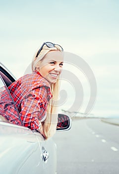 Happy smiling young woman looks out from car window
