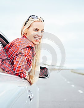 Happy smiling young woman looks out from car window