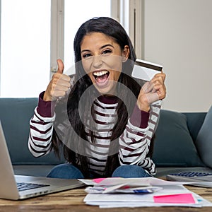 Happy smiling young woman making online payments bills using laptop and credit card and thumb up